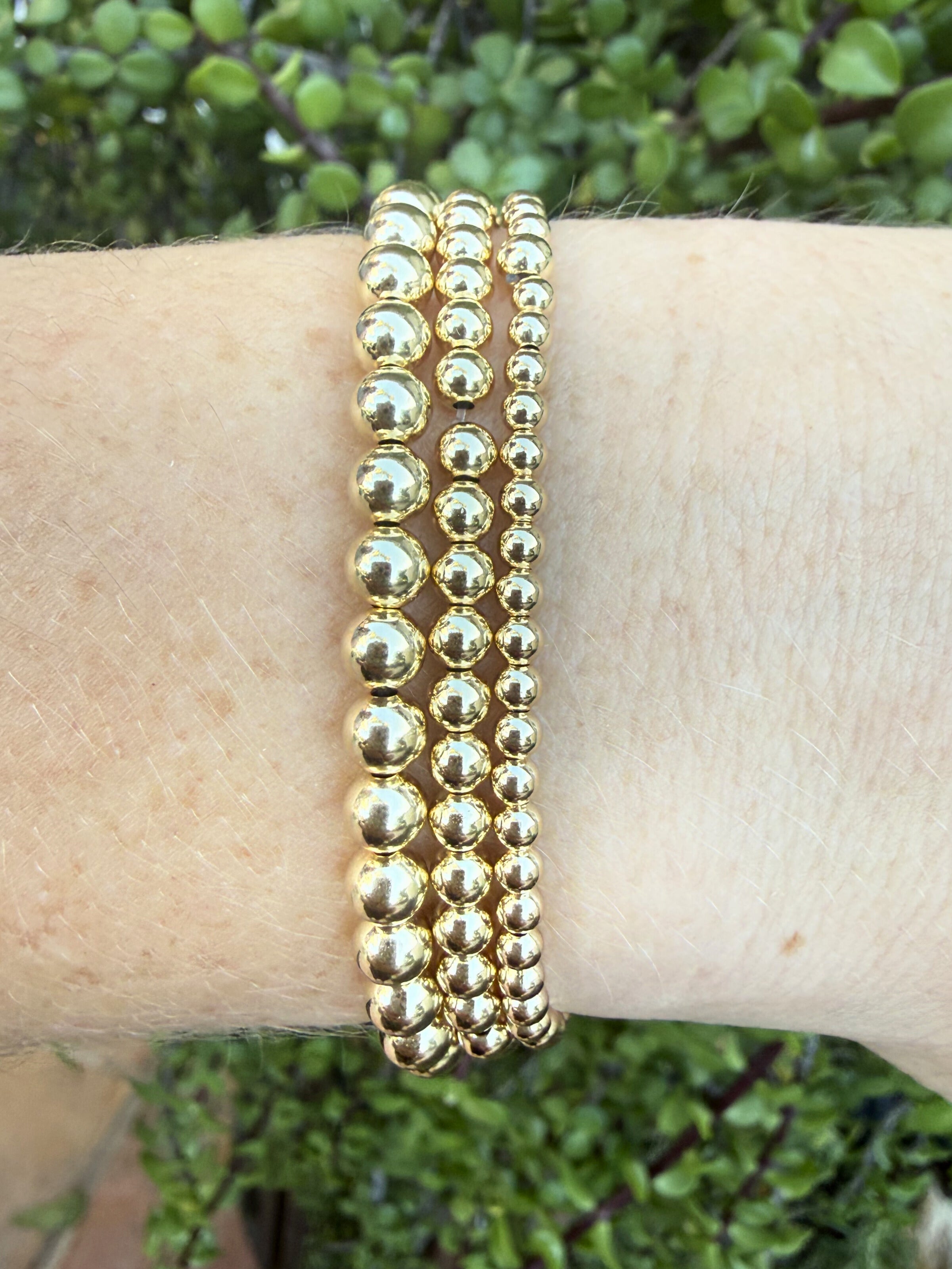 Gold beaded bracelet on a wrist with a green leafy background