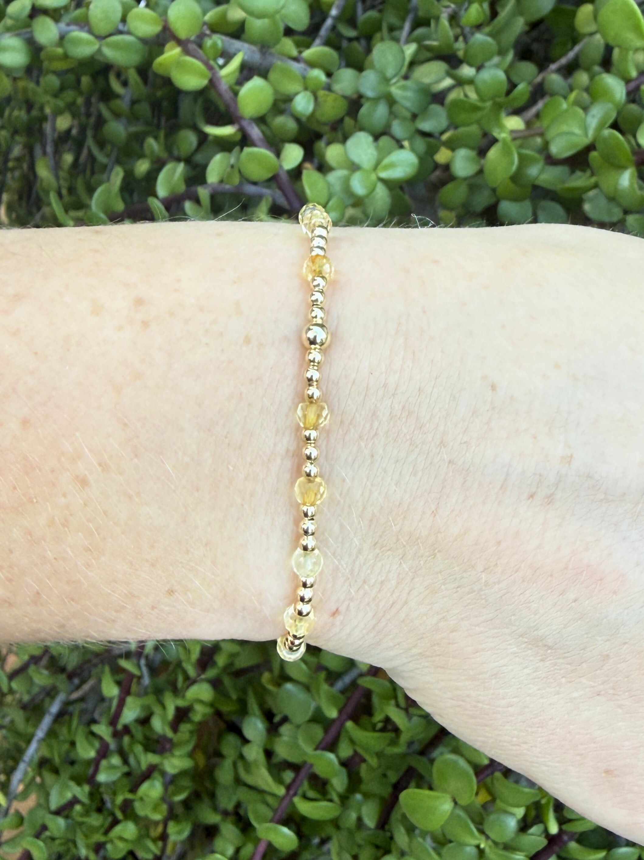 Gold beaded bracelet with citrine gemstone on a wrist with a green leafy background
