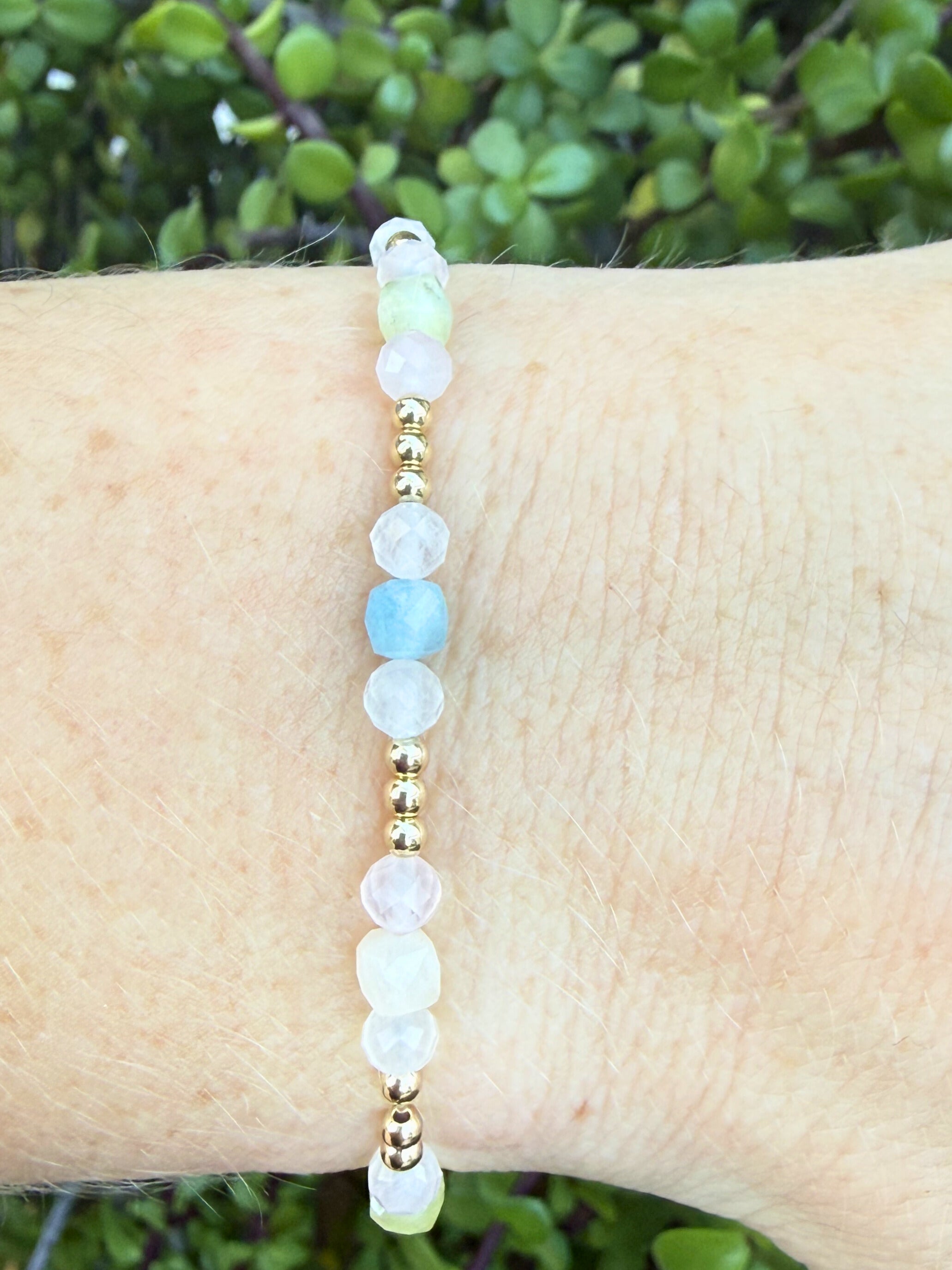 Bracelet with gold accents and light colored beads, rose quartz and morganite on a wrist against a natural background