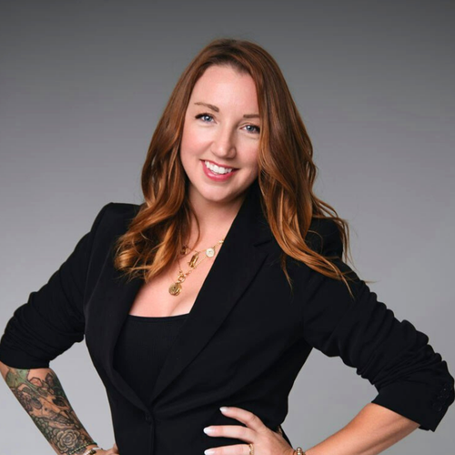 Woman in a black blazer with tattoos on arms against a gray background