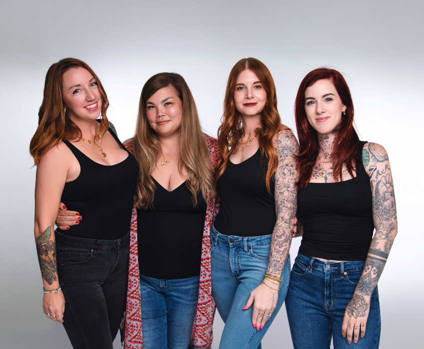 Four women with tattoos standing together against a plain background